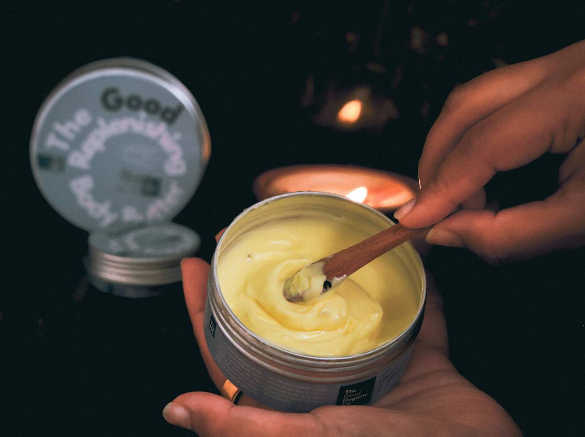 Hand holding a natural butter bar skin care product against a backdrop of dry skin texture